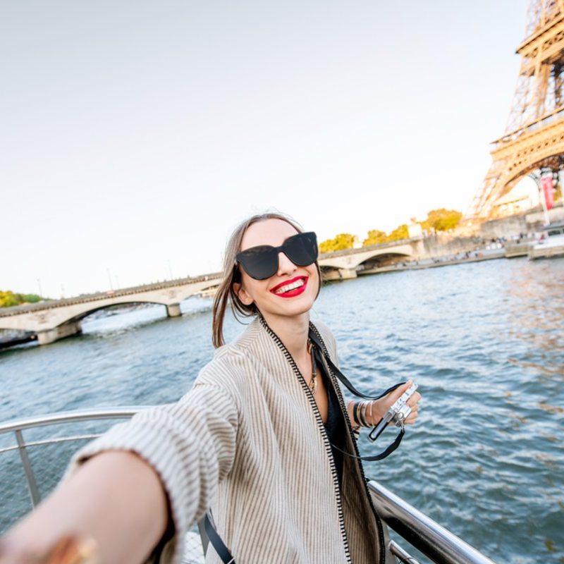 Young woman tourist making selfie photo with Eiffel tower on the background from the boat during the sunset in Paris